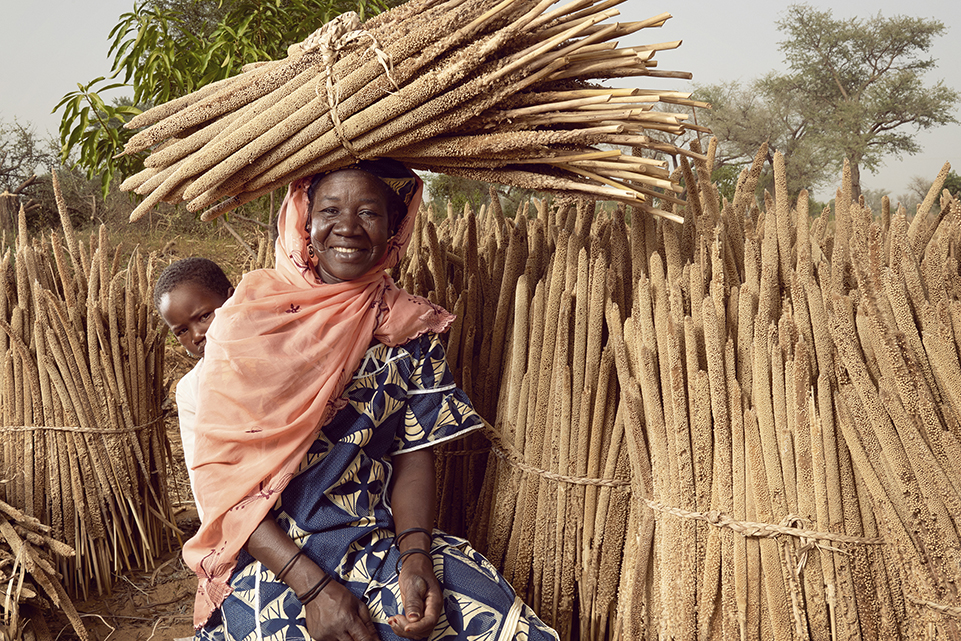 woman carrying bundle of stalks on her head, with child peeking out from behind her woman carrying bundle of stalks on her head, with child peeking out from behind her