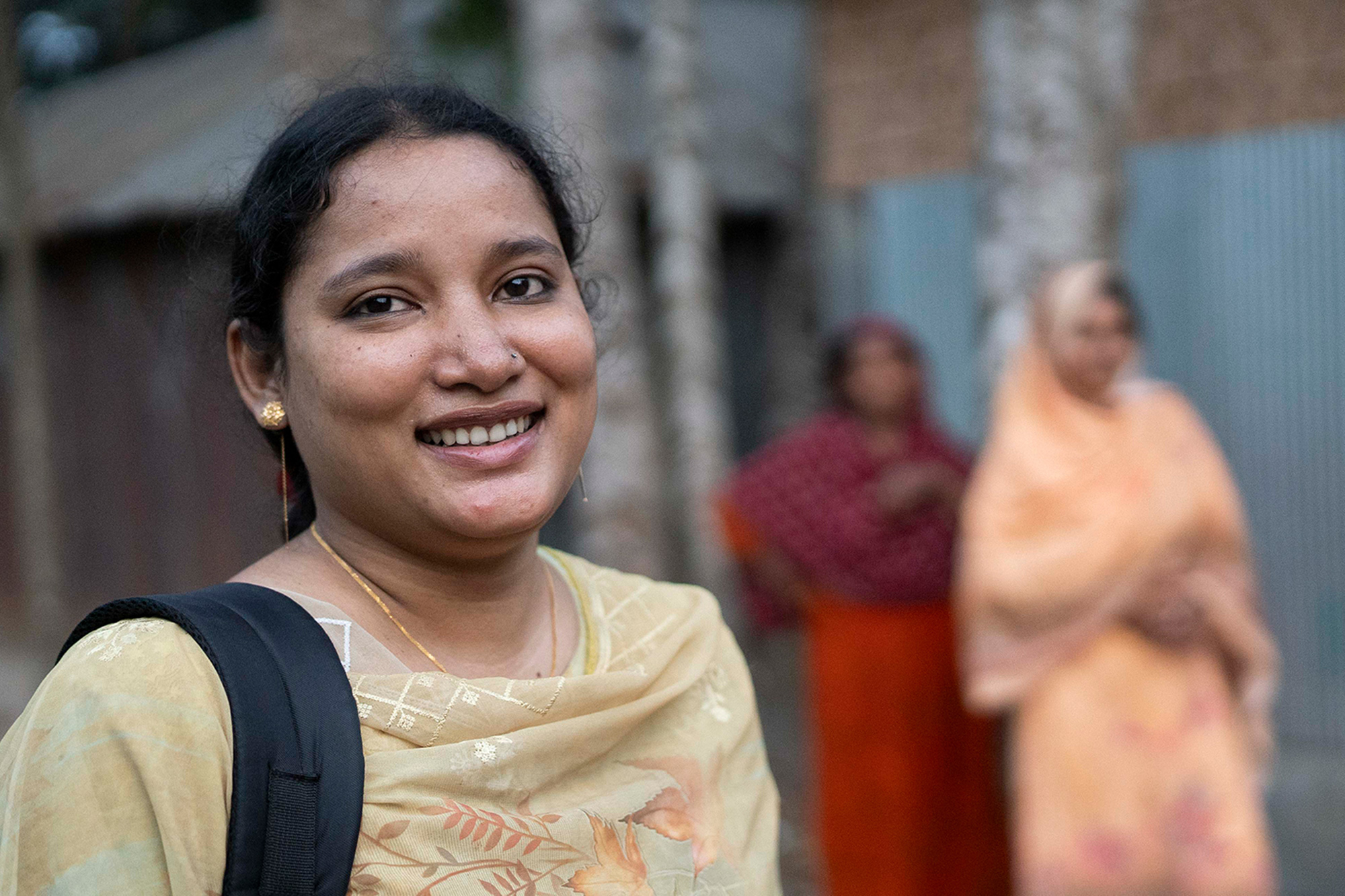 Young Bangladeshi farmer looking into the camera on the street with two blurred women in background.