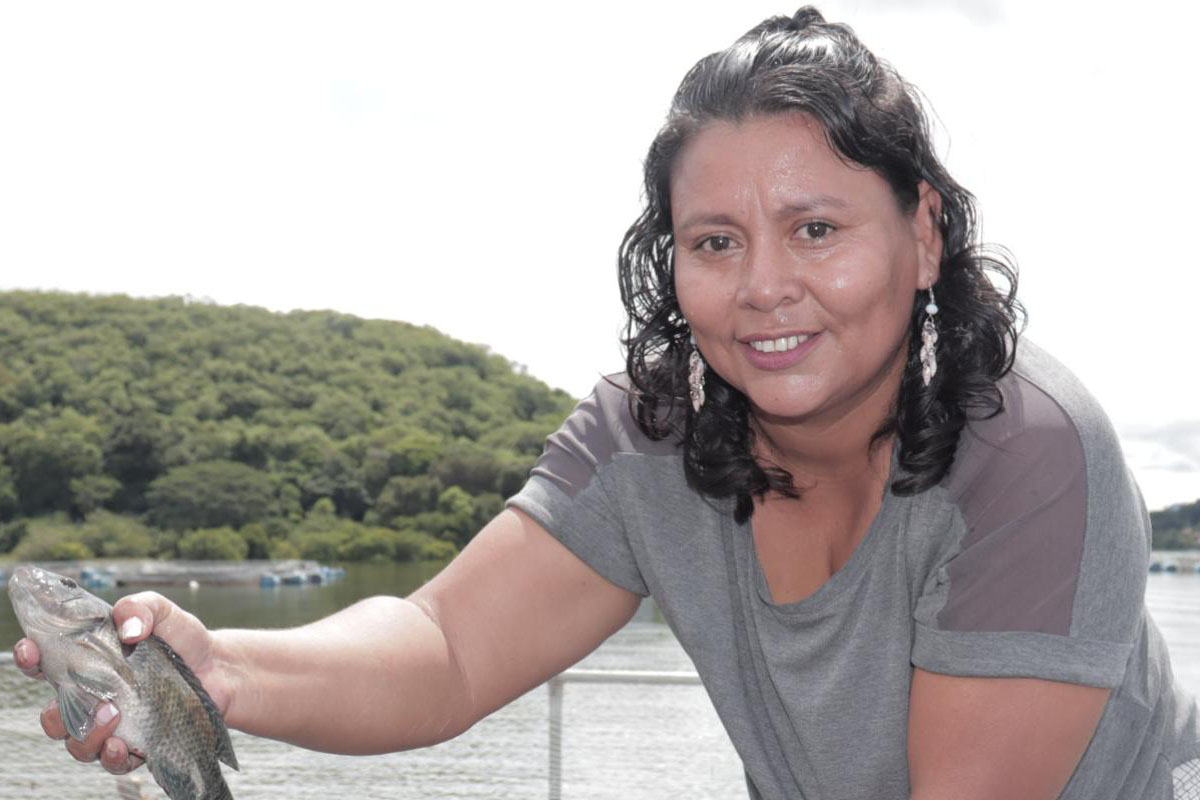 Lien vers le site de l'OIM Une femme sort un poisson d'une cage d'aquaculture.