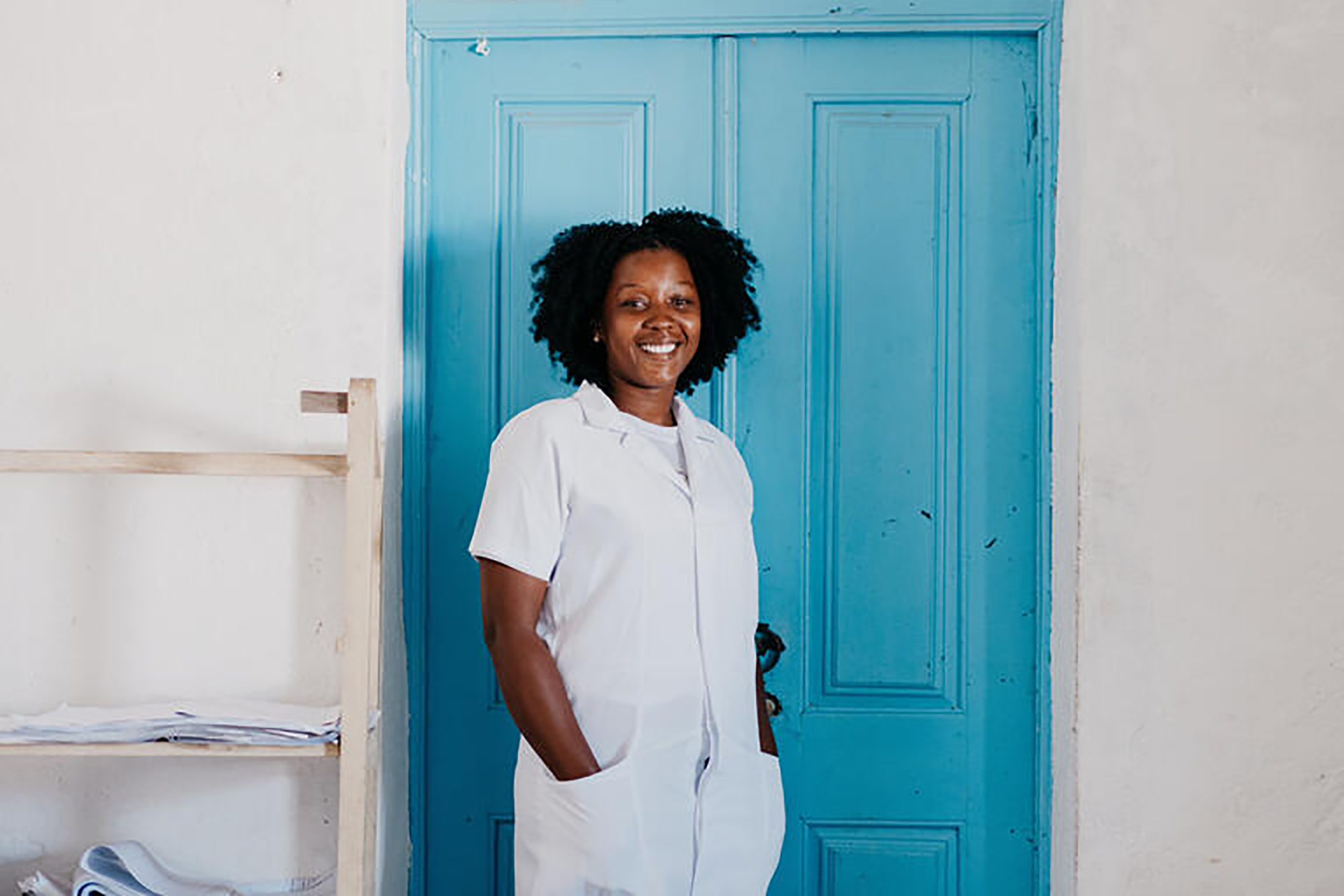 A woman smiling at the camera against a white wall and a blue door.